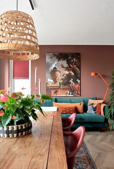 a beautiful muted colored living room with chocolate brown walls, a green sofa with orange pillows and a lamp, an artwork and a dining zone Art Deco Style Interior, Wood Centerpiece, Nordic Vintage, Wood Centerpieces, Green Sofa, Brown Walls, Brown Living Room, Home Lifestyle, A Living Room