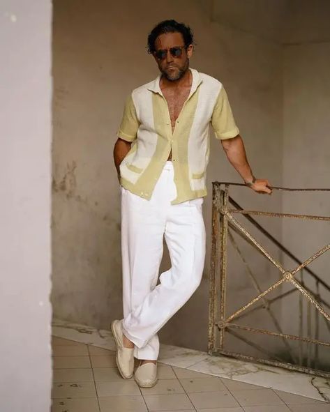 a catchy and chic beach wedding guest outfit with a printed yellow shirt, white trousers and neutral loafers