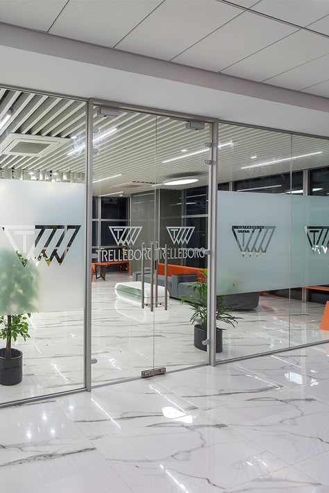 Glass Frosting can be a sure way of highlighting your branding at the workspace. When ZYETA designed the new Trelleborg's office space, the brand's logo was beautifully decorated on the glass doors, depicting brand marketing. #glassfrostingdesign #officeinteriors #workspacedesign #glassdoordecor Frosted Logo On Glass Door, Frosted Glass Office Doors, Glass Door Office Design, Office Window Design, Glass Film Design Office Patterns, Glass Sticker Design Office, Glass Paper Design, Office Glass Design, Office Glass Door Design