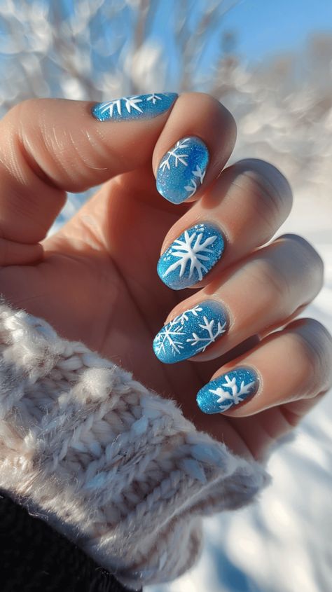 A manicured hand with icy blue nails with white snowflake designs representing Elsa from Frozen. Icy Snowflake Nails, Snowflake Nail Art Designs, Frozen Theme Nails, Blue Christmas Nail Art, Elsa Nails Frozen, Frozen Nails Disney, Xmas Nails Snowflake, Blue Winter Nails Short, Winter Disney Nails