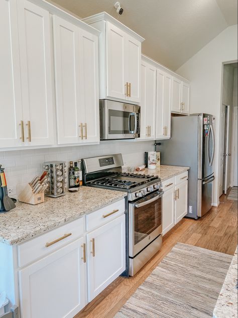 Brass pulls, white countertop, white subway, snowfall granite and wood floors White Cabinets Gold Hardware Kitchen, White And Gold Kitchen Decor, Gold Kitchen Appliances, White And Gold Kitchen Ideas, Gold Kitchen Decor, White Cabinets With Granite, Modern Gold Kitchen, Gold Kitchen Ideas, White And Gold Kitchen