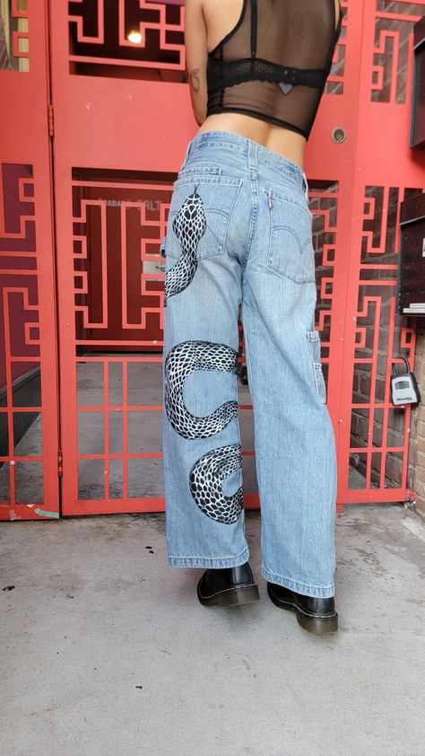 Painted snake pants Snake Jeans Painted, Painted Camo Pants, Diy Pants Paint Aesthetic, Jeans With Painting, Painted Denim Jeans Ideas, Mushroom Jeans Paint, Painted Pockets Jeans, Black Painted Jeans, Painting On Jeans Aesthetic