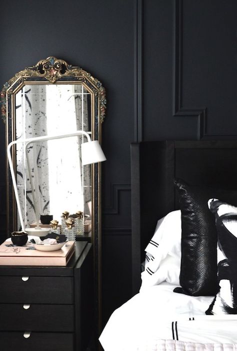 White and black bedroom features black walls adorned with black trim moldings framing a black wingback headboard on queen bed dressed in black and white hotel bedding as well as black and white pillows, Modern Circles Pillows, beside a black nightstand topped with an Ikea TISDAG LED Work Lamp in front of an antique mirror. Bedside Mirrors, White And Black Bedroom Ideas, Gustavian Bedroom, Bedside Styling, White And Black Bedroom, Christine Dovey, Nightstands Ideas, Mirrors Ideas, Black Bedroom Ideas