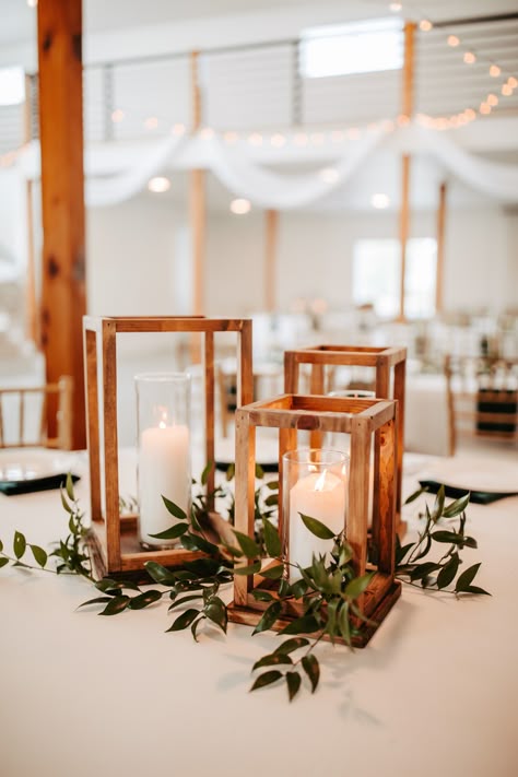 Rustic wooden rectangular candle holders for a fall centerpiece for the guest tables. Tables accent with white china plates, dark green satin napkins, and sprigs of greenery at this real indoor fall wedding reception at Emerson Fields in Missouri. Wedding Centerpiece Rustic Elegant, Simple Greenery Table Centerpieces, Centerpiece Rustic Wedding, Simple November Wedding Decor, Rustic Wedding Decor Eucalyptus, Wooden Candle Holder Centerpiece, Rustic Centerpiece Wedding Diy, Wedding Guest Table Decorations, Deep Green Wedding Table Decor