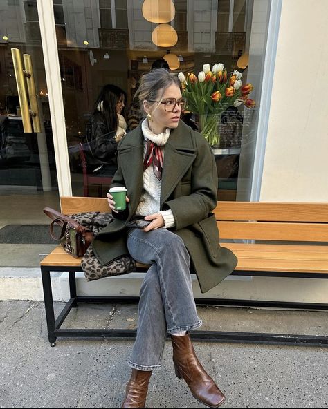 Parisian blond girl sitting on a bench with her coffee in hand. She is very in trend dressed. Her hair is up and is wearing brown squared glasses. She is wearing a thick white knitted turtleneck which she tied a thin elegant red satin  scarf around her neck. She associated this with grey jeans, brown leather block heels boots and a green jacket. Parisian Chic Style Fall, Colorful Winter Outfits, Green Jacket Outfit, Fall Jackets Outfit, Outwear Outfit, Winter Outfits Ideas, Cardamom Buns, Khaki Coat, Christmas Instagram