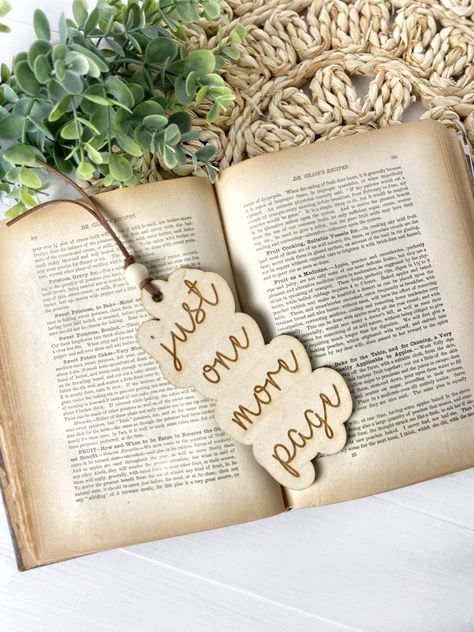 "These wooden bookmarks make a sweet and practical gift for those book lovers in your life.  Bookmark is made from maple wood, laser cut and engraved with the saying just one more page and measures approximately 2 1/2 x 6\". Adorned with suede cord and a bead. Choose if you want font 1 or font 2 in the drop down menu.  Check out our other bookmarks here https://www.etsy.com/shop/HillCoDesigns?ref=seller-platform-mcnav&section_id=41456012 Instant 15% off code when you sign up for our email list. Cricut Wood Engraving Projects, Best Fonts For Laser Engraving, Laser Engraved Bookmarks, Laser Cut Bookmark, Wood Laser Projects, Laser Gift Ideas, Laser Projects Ideas, Laser Engraving Ideas Gifts, Laser Engraver Projects