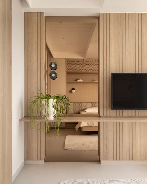 This guest bedroom exudes calm with light-toned finishes, featuring dyed oak wood veneer and beige textured laminate on wardrobes for added depth. The bed is designed to float above the floor, creating openness and maximizing space, while built-in shelves offer extra storage. Perforated shutters neatly conceal the AC unit, keeping the design sleek. A subtle green headboard adds a touch of color, complemented by custom bedside lights and built-in side tables. The paneled TV wall transitions in... Paneled Tv Wall, Bedroom Built Ins For Tv, Wardrobe Headboard, Hidden Vanity, Minimalism Interior Design, Vanity In Bedroom, Tiered Ceiling, Tv Feature Wall, Sons Room