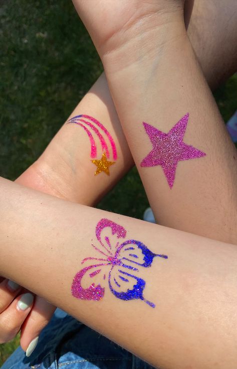 this pin shows three glitter tattoos on a group of peoples' arms. One tattoo is a pink star, one is a blue and pink butterfly, the last is a shooting star with a gold star and pink ombre lines. Glitter Tattoo Designs, Glitter Tattoo Temporary, Diy Glitter Tattoos, Glitter Tattoo Summer, Glitter Temporary Tattoos, Temporary Glitter Tattoo, Glitter Tattoo Aesthetic, Glitter Tattoo Permanent, Glitter Bar Ideas