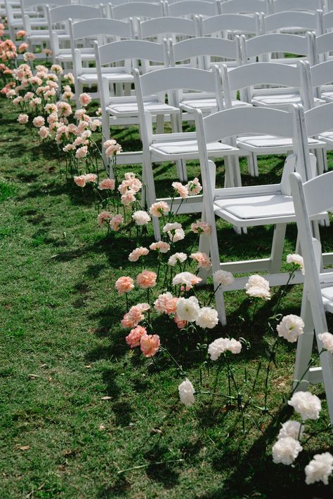 Pink and white florals lined up down the ceremony aisle with classic white chairs | ceremony details, ceremony inspo, ceremony florals, floral aisle Ribbon On Ceremony Chairs, Single Flower Aisle Wedding, White Chair Ceremony, Floral Ceremony Aisle, Single Stem Aisle Flowers, Flowers In Ground Wedding Aisle, Single Stem Aisle, Wedding Ceremony Set Up, Wild Flower Aisle