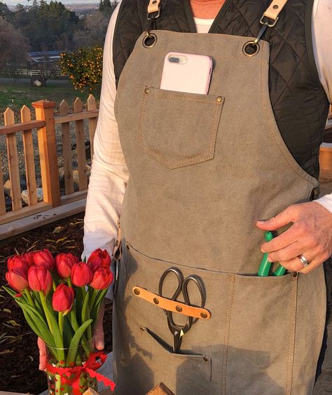 From our flower farm to your home and garden.  All items shipped from U.S. Relieves neck strain with cross back strap system. Our most popular item. This unique handpicked garden florists apron/smock is perfect for a day of gardening or in the floral shop.  It's cross back strap system reduces neck strain, and allows you to fill the pockets without neck strain.  Made from cool, soft waxed cotton canvas and leather accents, its perfect for pruning, potting, planting or any other gardening chore. Couture, Gardening Apparel, Florist Apron, Aprons With Pockets, Garden Apron, Garden Scissors, Holiday Inspo, Shop Apron, Work Aprons