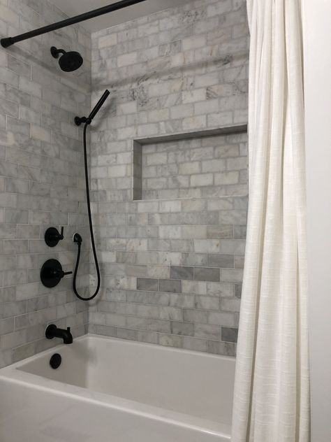 Farmhouse Shower Bathtub Combo - Matte Black Delta Fixtures with Floor and Decor Casa Antica Ocean Honed Marble Tile Redo Bathtub Shower Combo, Bathtub With Black Fixtures, Extra Long Tub Shower Combo, White Tub Black Fixtures, Tiling Around Bathtub Tub Surround, Tiled Tub Shower Combo Farmhouse, New Bathtub Shower Combo, Tub Shower Combo Remodel Farmhouse, Shower Tub Surround Ideas