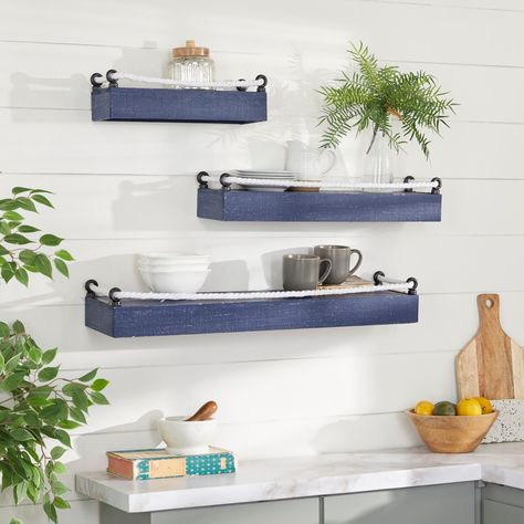 "Set of 3 Blue Wood Contemporary Wall Shelves Give new life to drab colorless walls with this 3-piece coastal style blue wood wall shelf. This beautiful set comes in 3 different sizes for all your decor and home organization needs. Each rectangular shelf platform features a white rope fasted to black metal hooks to help prevent objects from accidently falling off the shelves. The wood platforms come in a lively blue finish like the deep ocean to complement your costal style home wherever wall th Contemporary Wall Shelf, Knotted Rope, Metal Wall Shelves, Shelves Wall, Rope Shelves, White Rope, 3 Shelves, Wood Wall Shelf, Blue Wood