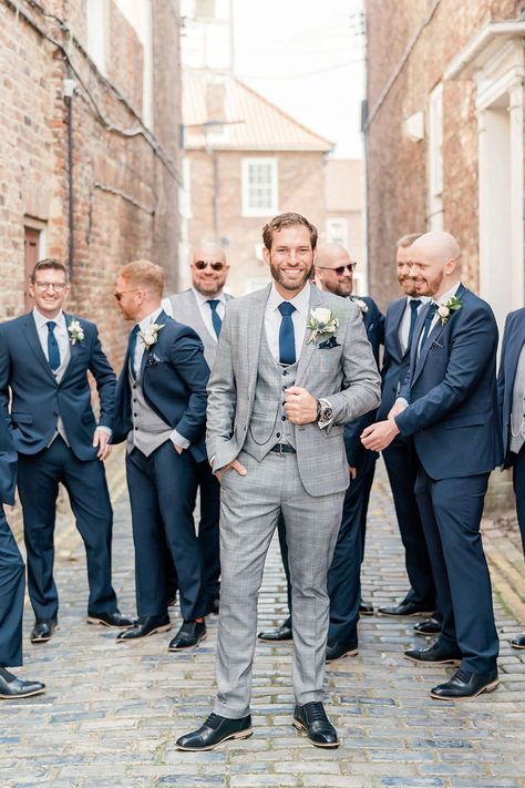 Groom in a light grey check wedding suit with his groomsmen in navy three-piece suits standing behind him | Caro Patrick Photography Grey Suits For Men Color Combos, Grey Suit Navy Tie Wedding, English Wedding Suits Men, Grey Groom Suit With Bride, Grey Suit With Navy Tie, Grey And Blue Suit, Grey Suit Blue Tie, Navy Grey Suit, Wedding Tuxedo For Men