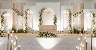 This image showcases an elegant and beautifully decorated wedding stage. The backdrop features a series of white panels adorned with lush green foliage and white floral arrangements, creating a serene and romantic ambiance. The central arch, framed with cascading flowers, highlights a pristine white sofa, perfect for the bride and groom. The stage is further enhanced by modern, artistic light fixtures and tall, golden candle stands, adding a touch of sophistication and warmth to the setting. ... Wedding Sofa Decoration, White Stage Decor, Wedding Stage Decorations Elegant, Wedding Stage Ideas, Sofa Wedding, Weddings Decorations Elegant Romantic, Golden Candle, Wedding Cupcakes Rustic, Floral Sofa