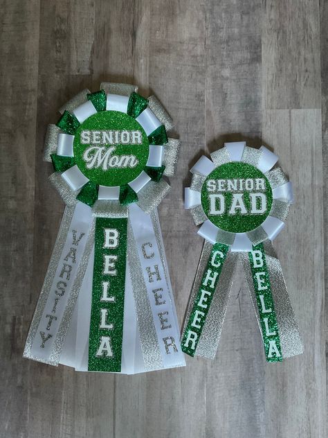 Make your Senior Cheerleader's Parents feel special with Senior Mom & Senior Dad Pins for Parent's Night or Seniors Night. This set includes a Senior Mom Pin and Senior Dad Pin with the Cheerleader's name on it. You pick your glitter color from the swatch pictures.  **NO REFUNDS OR EXCHANGES- these items are made to order with your colors and mascot/school so they will not be able to be returned/exchanged/refunded. Please make sure you input carefully your choices in colors and spelling of name. I will use the exact spelling you give me. If you have special requests or questions please message prior to placing order.  **All items are handmade and may have slight imperfections**   **Actual colors of ribbon and vinyl may vary from screens of electronic devices so use swatch pictures only as Senior Mom Gift Ideas, Senior Night Ideas Cheerleading, Senior Night Cheer Gifts, Cheer Senior Night Ideas, Senior Night Gift Ideas Cheerleading, Football Senior Night Ideas, Senior Recognition Ideas, Senior Cheer Gifts, Cheer Senior Night