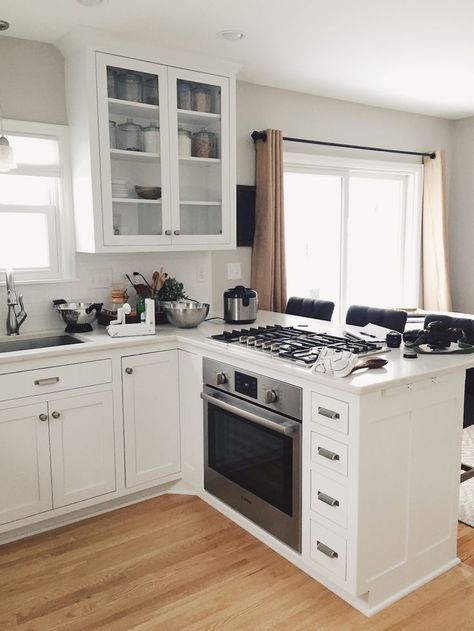 White kitchen with glass door display cabinet and peninsula with oven and cooktop. Kitchen Layout With Peninsula, Mv Ideas, Island With Stove, Kitchen Island With Stove, Kitchen With White Cabinets, Craftsman Remodel, Decor Cabinet, Kitchen Peninsula, Best Kitchen Design