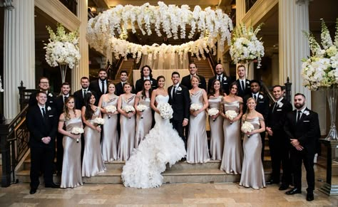 The bride and groom were joined by groomsmen in suits and orchid boutonnieres, as well as bridesmaids in sleek champagne-hued gowns featuring draped necklines. Large Bridal Party Ceremony, Huge Wedding Party, Large Bridesmaid Party, Wedding Photo Ideas Large Bridal Party, Large Bridal Party Photos, Large Bridal Party Pictures, Groomsmen In Suits, Large Wedding Party Photos, Wedding With White Flowers