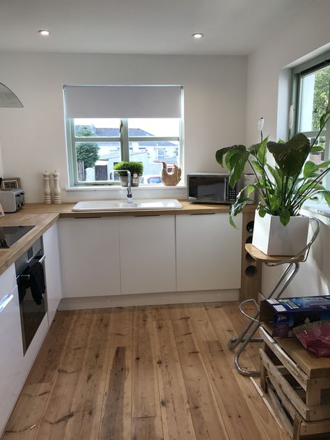 Natural kitchen theme. Ceramic white sink, oak tops, pine floorboards and gloss white doors with hidden flush handles.. and a Peace Lily to top it all off #kitchen #freshkitchen #neutralhome #floorboards #cottagekitchen #oakworktop #glosswhite White Kitchen Wooden Floor, Cream And Wood Kitchen, Slab Door Kitchen, Galley Kitchen Lighting, Pine Floorboards, Gloss Kitchen Cabinets, Kitchen Refurbishment, White Gloss Kitchen, Kitchen Revamp