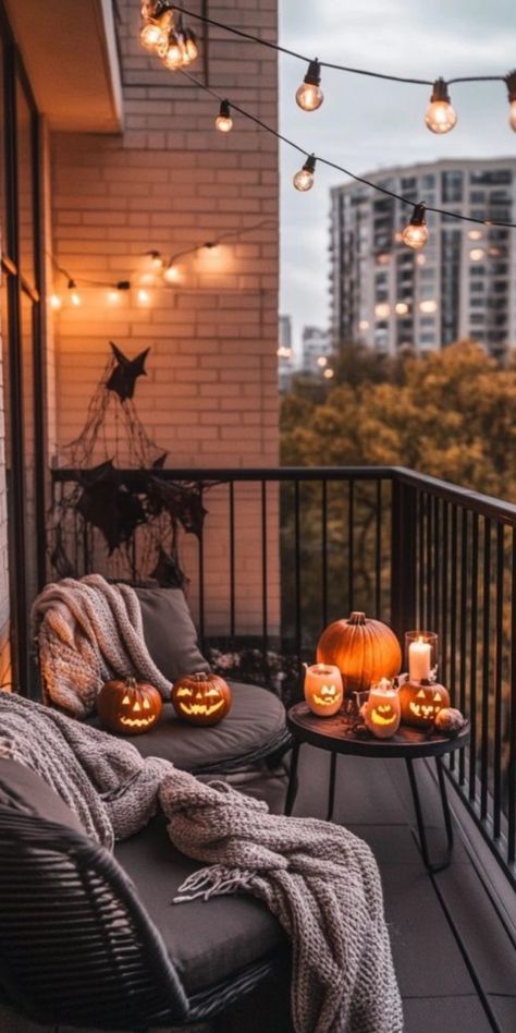 Cozy balcony decorated for Halloween with string lights, carved pumpkins, and blankets. Balcony Autumn Decor, Fall Decorations Apartment Small Spaces, Apartment Decorating Halloween, Apartment Balcony Fall Decor, Ugly Apartment Decorating Rental, Fall Apartment Patio Decor, Apartment Balcony Decor Ideas, Patio Decorating Ideas For Apartments, Halloween Apartment Decor Balcony