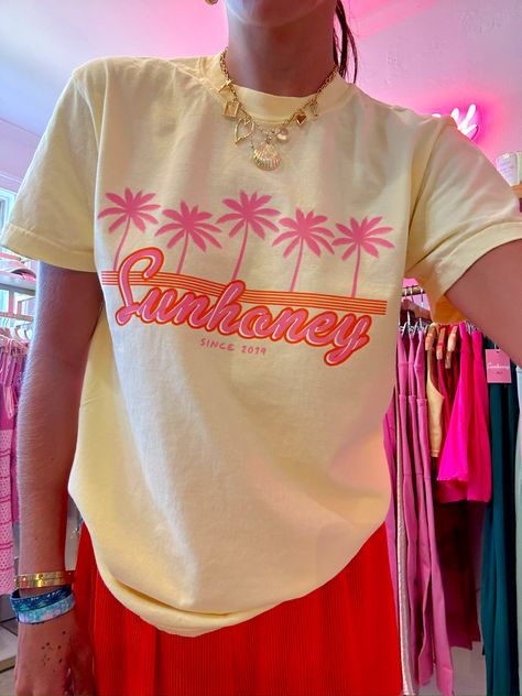 Our EXCLUSIVE Sunhoney Retro Palm Tee in Yellow screams summer vibes with its playful graphic of pink palm trees and orange retro design. Featuring our classic logo in a stunning orange and pink colorway, this tee is the perfect addition to your warm weather wardrobe. This summer graphic is printed on Comfort Colors tee and is a full length, shirt is tucked in for photos for styling purposes. Get yours now and be prepared to wear all summer long! Product is made to order: available for pick up/s Summer Tee Shirt Designs, Tropical T Shirt Designs, Print On Demand Clothing, Graphic Shirt Design Ideas, Retro Tshirt Design Graphics, Preppy Graphic Tees, Retro T Shirt Designs, Light Yellow Shirt, Oversized Tshirt Outfit Summer