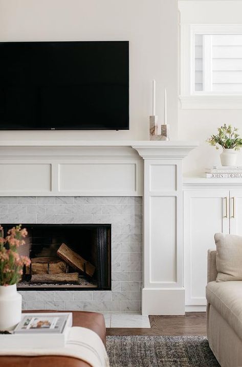 Gray marble subway tiles are framed by a white mantel topped with pink and gray marble candle holders and positioned under a wall mount TV. Fireplace On Flat Wall, White Fireplace Mantel, Subway Tile Fireplace, White Fireplace Mantels, Traditional Fireplace Mantel, Grey Stone Fireplace, Fireplace Feature, Stone Fireplace Wall, Built In Around Fireplace