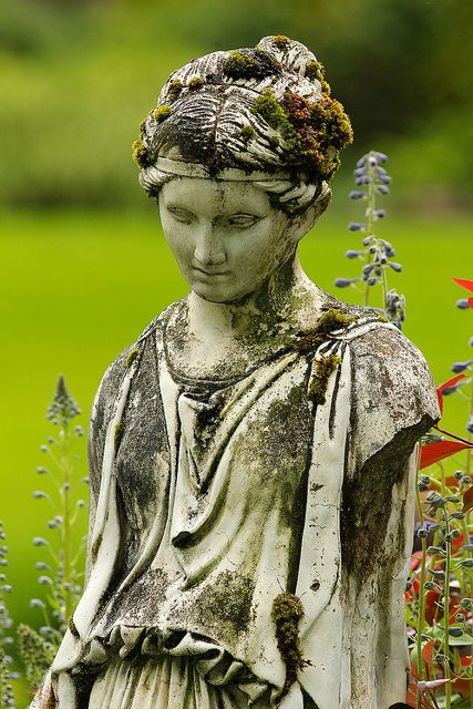 An old statue, who's arms had been knocked off long ago, is now a home for moss and lichen, among other living things. Green Statues Aesthetic, Moss Covered Statues, Mossy Statue Aesthetic, Mother Nature Statue, Statue Covered In Moss, Statue Fountain, Living Statue, Garden Figures, Mermaid Statues