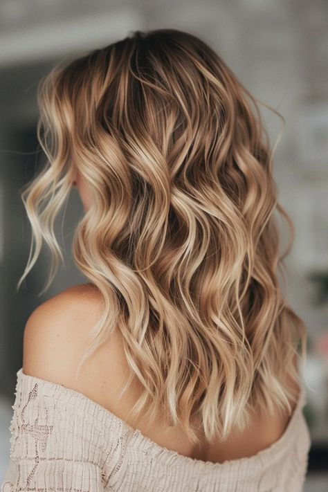 Blonde wavy hair cascading over shoulders against a soft-focus background. Soft Honey Blonde Balayage, Neutral Toned Blonde Hair, Almond Butter Blonde Hair, Vanilla Almond Butter Blonde Hair, Warm Vs Cool Blonde, Ashy Lowlights, Teddy Bear Blonde Hair, Champagne Balayage, Winter Highlights For Blondes