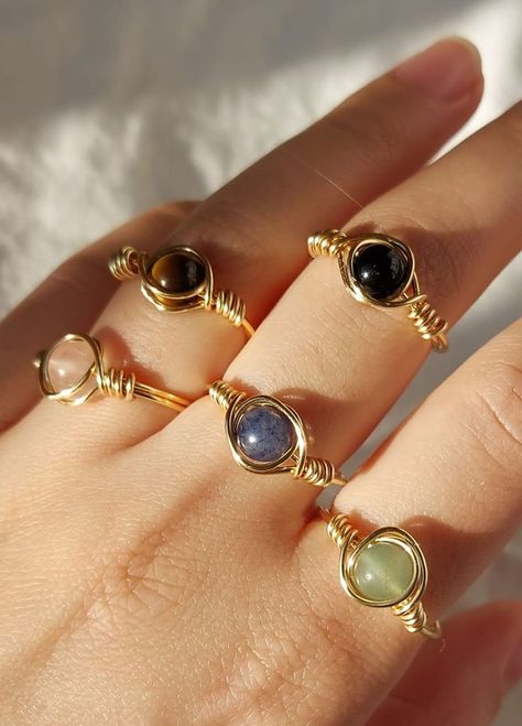 A hand wearing multiple handmade wire wrapped rings with crystal gemstones. Crystal Wrapped Rings, Wrap Around Rings, Ring With Stone Design, Wire Rings With Stones, Wire Bracelet Diy, Amythest Jewelry, Handmade Rings Wire, Wired Ring, Crystals Rings