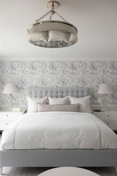 Clean traditional bedroom with blue and white patterned wallpaper, a light blue bed with white bedding and a tufted headboard, white sidetables flanking the bed, and a large round mirrored light fixture above the bed Master Bedrooms Wallpaper, Pale Blue And Cream Bedroom, Light Blue Bed Frame, Wallpaper Master Bed, Blue And White Wallpaper Bedroom, Blue Wallpaper Bedroom Ideas, Round Mirror Above Bed, White Patterned Wallpaper, Bedroom Inspirations Wallpaper