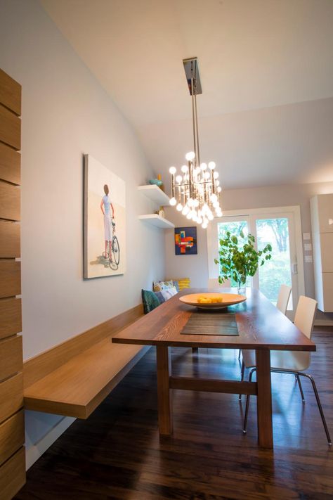 A floating bench built into the wall creates unique seating along the wood dining table. Wall art adds color and decoration while keeping with a polished, minimalist look. A contemporary light fixture features a metal form with small circular bulbs joining with the natural light from the french doors to brighten the space. Floating Banquette Seating, Wall Bench Seating, Long Wood Table, Midcentury Dining Room, Bench Seat Dining, Bench Seating Kitchen, Banquette Seating In Kitchen, Wall Bench, Banquet Seating