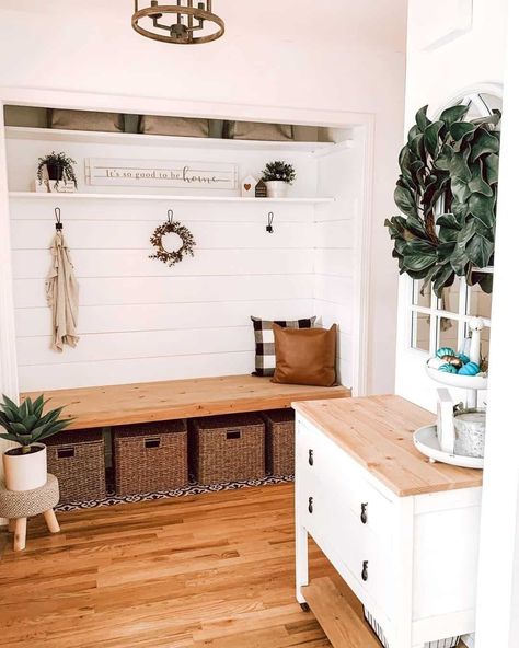 A rustic farmhouse mudroom is styled with a warm wood bench with rattan storage bins stowed below and shelving adorned with farmhouse decor above. Hooks are mounted on a white shiplap wall and accent pillows adorn the bench. A white console table with a light wood top rests adjacent and potted greenery is displayed on a light wood stool next to the bench. A wreath of greenery adorns the mirror above the console table...   Image: myfirst_farmhouse White Beadboard Walls, Bench With Baskets, Dark Tile Floors, Modern Farmhouse Mudroom, Beadboard Wall, Farmhouse Mudroom, Warm Wood Flooring, White Beadboard, White Console Table