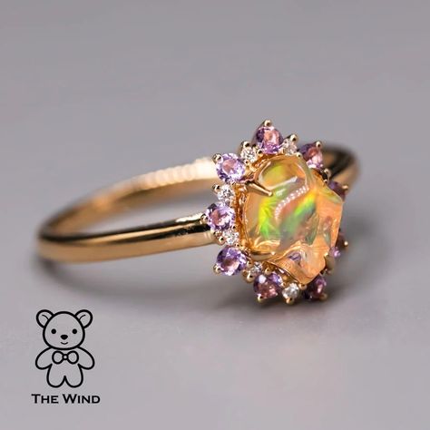 Hey everyone! Today, let me introduce the Mexican Fire Opal Amethyst Diamond Engagement Halo Ring in 18K Yellow Gold. Designed by our artist for someone truly special, this unique ring features a circle of amethyst embracing the Mexican Fire Opal. Ideal for engagements and anniversaries, its uniqueness ensures you won't find a match. Express your love uniquely! 💖 #EngagementRing #uniquelove #OpalJewelry #OpalLove #DiamondRing #FineJewelry #JewelryLove #Ring #JewelryMagic #DiamondHalo #LuxuryF... Opal And Diamond Wedding Ring, Fire Opal Wedding Ring, Opal Sapphire Ring, Whimsy Rings, Gold Opal Rings, Rarest Gemstones, Opal And Sapphire Ring, Opal Promise Ring, Mexican Fire Opal Ring