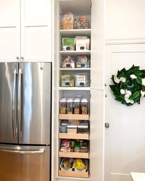 This vibrant kitchen features a large stainless steel refrigerator and bright white cabinets adorned with a leafy wreath. A narrow pantry is built into the wall and displays rows of clear bins with neat labels. Turn a small space in your kitchen into a pantry with stackable bins and canisters, and use labels to keep everything tidy. Narrow Kitchen Storage Ideas, Small Pantry For Small Kitchen, How To Add Pantry To Small Kitchen, Narrow Pantry Storage, Small Space Pantry Cabinet, Long Narrow Kitchen Cabinet Storage, Pantry In The Wall, Narrow Space Next To Refrigerator, Organisation