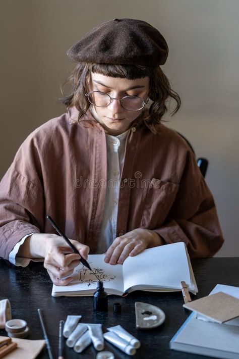 Young focused female artist wearing beret and glasses sitting at table painting with black ink stock photos Sitting At Table, Table Painting, Female Artist, Wearing Glasses, Painted Table, Art Therapy, Female Artists, Stock Images, Stock Photos