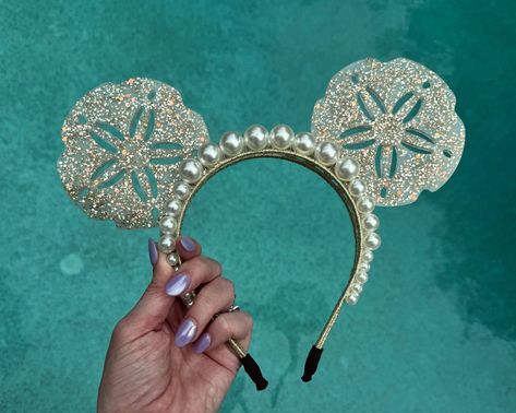 For all my mermaid girlies! These resin sand dollar mouse ears are neutral yet show stopping at the same time. The mouse ears headband is accented with 2 rows of oversized pearls, and the resin sand dollars sparkle with gold flecks and gold glitter. A perfect complement to any mermaid outfit or Ariel inspired look for the parks, these ears are mer-made for you :). Due to the handmade nature of my ears and the artistic quality of resin, each pair will vary slightly, making yours unique and just f Disney Cruise Ears, Avatar Ears, Resin Sand, Pearl Princess, Diy Disney Ears, Diy Mickey Ears, Hello Holiday, Disney Headbands, Disney Mickey Ears