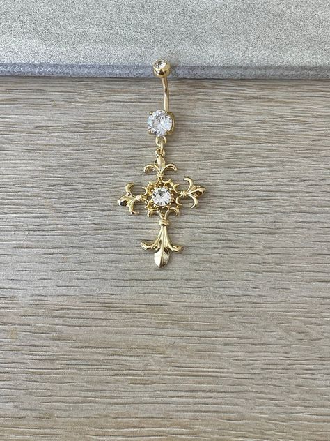 This gold cross belly button ring is beautiful and ornate. Made with surgical steel and coated in 14k gold, this belly button ring dangles with a beautiful cross charm, giving it a gorgeous sparkle, and making it practical for everyday wear. Perfect belly button / navel piercing. Drop jaws with this body jewelry. Details & Size: ♥ 316L Surgical Steel, 14k gold plated // Silver Option now available too! Silver option is surgical steel, not gold plated ♥ Cubic Zirconia Gems ♥ 10mm bar, 14G ♥ Externally Threaded ♥ Every purchase comes with an Elara gift box For sanitary purposes, piercing items are non-returnable, so please double check sizing and message me if you have any questions! Gold Cross Belly Button Piercing, Gold Piercings Belly, Belly Piercing Jewelry Gold, Cross Belly Ring, Belly Piercing Dangle, Belly Ring Gold, Cross Belly Piercing, Gold Belly Piercing Aesthetic, Belly Button Piercing Jewelry Gold