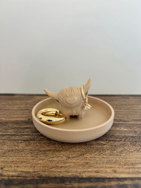 Elevate your jewelry organization with our Highland Cow Ring Holder, a charming addition to your decor that seamlessly blends farmhouse and bohemian flair. This cute ring display is more than just an organizer; it's a delightful piece of functional art. 🎁 Product Details: Material: High-Quality Marble PLA plastic Dimensions: Length 3.5 inches x Width 3.5 inches x Height 3 inches Color: Elegant Marble White 🌎 Conscious Crafting: We take pride in our environmentally conscious approach. Our items are 3D-printed with eco-friendly materials. 📸 Please Note: Accessories in Photos Not Included The product images may showcase accessories or additional items for decorative purposes only. Please be aware that the Ring/Earrings featured in the photos are not included with the purchase of the Bunny Highland Cow House Decor, Cow Room Decor, Cow Clay, Pottery Ring Holder, Jewellery Holder Clay, Air Dry Clay Ring Holder, Ring Holder Clay, Ceramic Ring Holder, Pottery Jewelry Holder