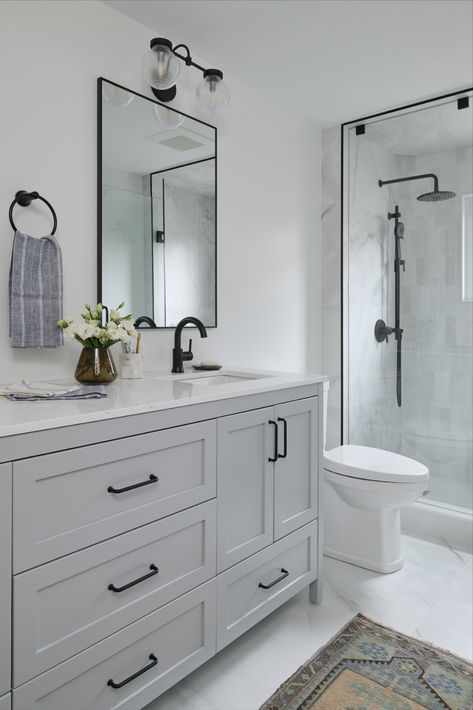 White washroom with warm grey double vanity and black plumbing fixtures with tiled shower and glass enclosure Farmhouse Washroom, Black Plumbing Fixtures, White Washroom, Black Hardware Bathroom, Black Bathroom Fixtures, Light Grey Bathrooms, Grey Bathroom Cabinets, Gray And White Bathroom, Grey Bathroom Tiles