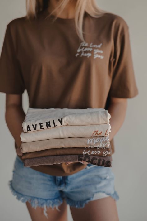 Girl holding stack of shades of brown and mocha graphic tees by Dear Heart Christian Fashion Outfits, Scripture Clothing, Church Shirt Designs, Christian Sweatshirts, Christian Clothes, Wildflower Drawing, Modest Wardrobe, Christian Shirts Designs, Cool Shirt Designs