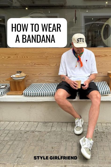 image of a man sitting on a bench wearing a white baseball cap, white t-shirt, orange patterned bandana around his neck, dark shorts, and Nike sneakers. Text on-screen reads: how to wear a bandana Guys Bandana Style, Men Neckerchief Outfit, Men Summer Scarf, Bandana Scarf Outfit Men, Neckerchief Outfit Men, Men Bandana Style, Neck Bandana Outfit, Bandana Outfit Men, Men Neckerchief