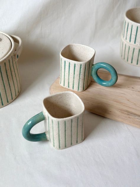 Ceramic Handmade Clay Mugs These ceramic mugs are perfect for sipping your favorite hot beverages. Each mug features a speckled finish with vertical stripe details, boasts a standout turquoise handle, adding a pop of color. Crafted from durable materials, they're kilned at high temperatures for strength and longevity. Food-safe and easy to clean, they're ideal for daily use or special occasions. With their handcrafted aesthetic, they make for a thoughtful gift or a delightful addition to your own kitchen collection. *Fired at a high temperature of 2200oF (1200oC) for durability. *Safe for drinking, and can be used in the dishwasher and microwave. Specifications: *Mugs hold 11.5 oz (approximately 350 ml). These mugs are part of the Bowl-Baking Dish collection. If you would like to explore t Creamic Mug, Handles Ceramic Mugs, Ceramic Mug Handles Design, Cute Pottery Mug, Hand Made Ceramic Mug, Ceramic Cup Handles, Handleless Mugs Ceramics, Cute Pottery, Speckled Mug