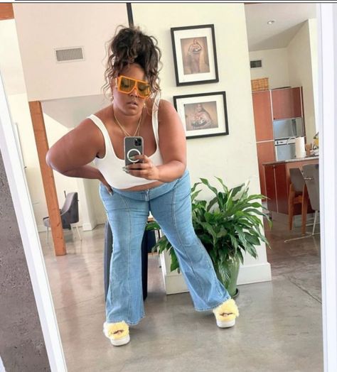 Lizzo taking a selfie wearing a white tank top, light wash wide leg jeans with a center seam, fuzzy yellow platform sandals, oversized orange aviators, and a messy top knot Lizzo Outfits Casual, Lizzo Aesthetics, Lizzo Outfit, Cheerleading Hairstyles, Maximum Effort, Cafe Society, Perfect People, Female Rappers, Beauty Icons