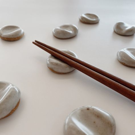 "These handmade ceramic chopstick or paintbrush rests are designed to look like a pebble or stone, adding an organic look to your table or desk. The design is simple, yet versatile, and can be used as a paintbrush rest, chopstick rest, pen holder, or even a worry stone. ☼ PRODUCT DETAILS ☼ * Each rest measures about 1.5\" round * Hand molded for an organic look * Stoneware clay * Warm off-white matte glaze with dark speckles * Food and dishwasher safe ☼ CHOPSTICKS AVAILABLE AS ADD-ON ☼ * If sele Diy Chopstick Rest, Air Dry Clay Chopsticks Rest, Ceramic Chopstick Rest, Chopstick Holder Ceramics, Clay Chopstick Rest, Chopstick Rest Ceramics, Clay Chopstick Holder, Ceramic Chopstick Holder, Small Ceramic Projects