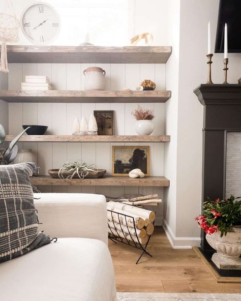 Stained wood farmhouse living room shelves are mounted to a vertical white shiplap accent wall. White, black and tan decor adorn the shelves in this living room featuring a black fireplace. Floating Black Shelves Living Room, Farmhouse Living Room Shelves, White Shiplap Accent Wall, Accent Wall White, White Sofa Living, Tan Decor, Shiplap Living Room, Cabin Basement, White Sofa Living Room