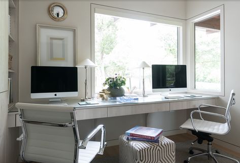 White task chairs sit on either side of a white and gray cube stool and at a light gray oak built-in desk fixed beneath a window. Built In Desk Under Window, Built In Office Desk, Desk Under Window, Built In Office, White Floating Desk, White Lacquer Desk, Blue Geometric Wallpaper, Den Library, Slate Tile Floor