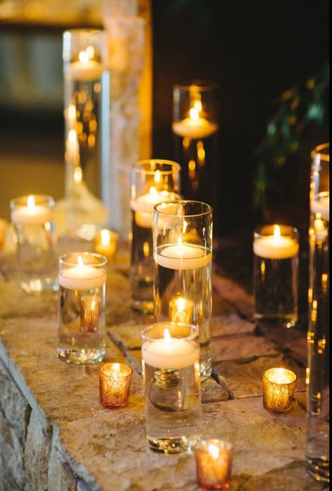 Collection of different sized candles in the fireplace. Candles In Bottles Wedding, Wedding Fake Candles, Tea Lights In Water, Covered Candles Wedding, Candles Reception Wedding, Enclosed Candles Wedding, Fake Candle Centerpieces, Fake Candles Wedding, Candles On Water