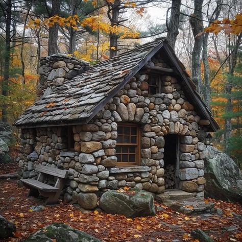 The image is of a small, rustic stone cottage nestled in a forest. The cottage has a fieldstone foundation and walls with a chimney made of the same material. The roof is made of rough-cut wooden shakes. The front door is made of wood. There is a small window on the right side of the cottage. The cottage is surrounded by trees and shrubs. The leaves on the trees are turning brown and orange, which suggests that it is autumn. Stone House In Forest, Small Stone Cottage Interior, Small Cottage Exterior Ideas, Stone Houses Rustic, Fieldstone Foundation, Stone Cottage Interior, Small Cabin Exterior Ideas, Tiny Stone Cottage, Hagrid Hut