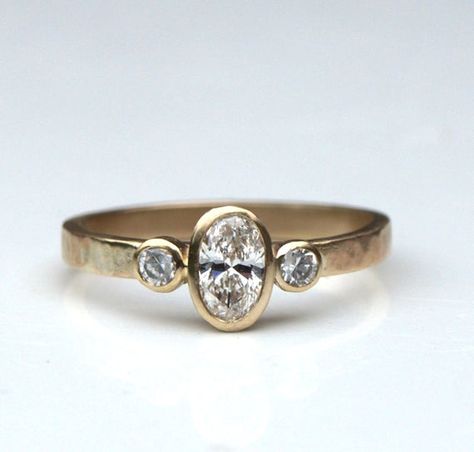 A lovely oval diamond trilogy ring. This one was made in recycled 9ct yellow gold but you can have any metal, just ask for a quote. ( Yellow and white gold are recycled, platinum isn't at present). The band has a textured finish but can also be smooth. The lovely central diamond is  6x 4mm oval, 0.37ct, flanked by two 2mm round diamonds (0.035ct each). The setting allow another ring to sit flush against this one and the low height makes it very practical. The band is 2mm wide.The ring is made to Flush Setting Engagement Ring, Wide Band Oval Engagement Ring, Three Stone Bezel Engagement Rings, Compulsory Heterosexuality, Low Setting Engagement Ring, Flush Ring, Diamond Trilogy Ring, Infinity Diamond Ring, Ring Inspiration