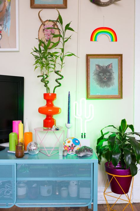 The orange plant stand and pink pedestal are both made by Eric Trine and the blue TV stand is from IKEA. Tv Stand Decor Colorful, Tv Stand Maximalist, Wavy Tv Stand, Tv Stand Colorful, Orange Tv Stand, Colored Tv Stand, Colorful Tv Stand, Pink Tv Stand, Cute Tv Stand