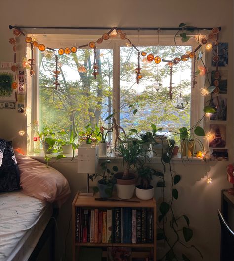 Picture of bed next to window with flower and orange garland hanging from curtain rod with plants on the windowsill. College Dorm Room Ideas Cottagecore, Cute College Dorm Decor, Dorm Aesthetic Retro Vintage, Earthy Dorm Room Ideas Vintage, Dorm Window Decor, Overhead Bed Decor, Cozy Room Fall, Dorm Room Ideas Plants, Cosy Dorm Room